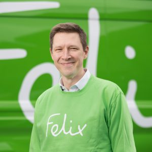 Headshot of Matt Birch smiling at camera wearing green jumper with Felix logo and standing in front of Felix branded van
