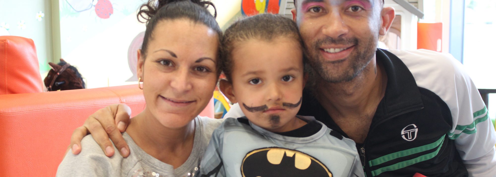 Mum, dad and son smiling at the camera. Son is dressed as batman.
