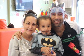 Mum, dad and son smiling at the camera. Son is dressed as batman.