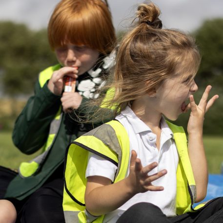 Children in hi-vis at a holiday club eating a picnic outside