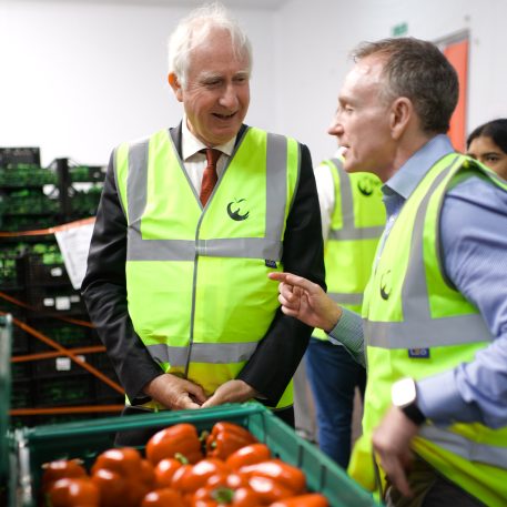 Minister of State for Food Security and Rural Affairs Daniel Zeichner with FareShare CEO George Wright. They are in a FareShare South West warehouse in Bristol, both wearing FareShare hi-vis, and are talking to each other over a pallet of vegetables.