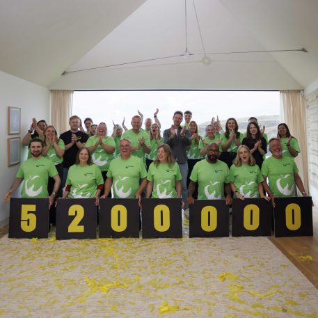 Photo from the reveal of the total raised, the crowd are wearing FareShare t-shirts and there are cards with the numbers showing £5.2 million. The crowd are smiling, clapping and cheering.