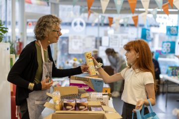 An older woman hands a young girl a tin of food in a community shop