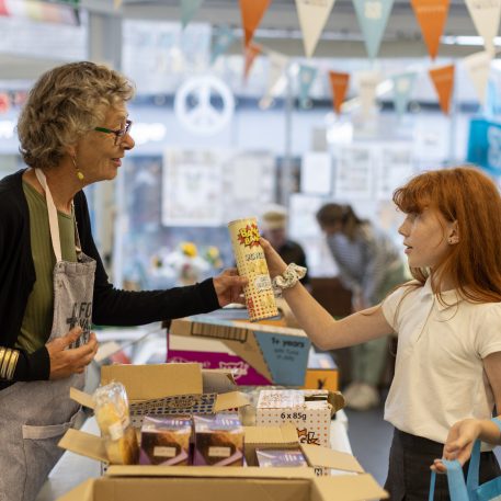 An older woman hands a young girl a tin of food in a community shop